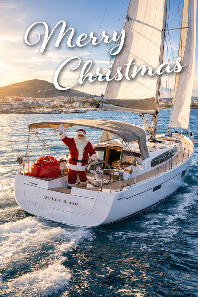 Santa in red suit on sailboat with 'Merry Christmas' text, sailing near city shoreline at sunset.